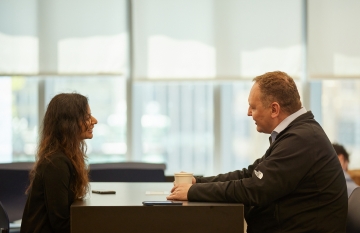 Two people talking at a desk.